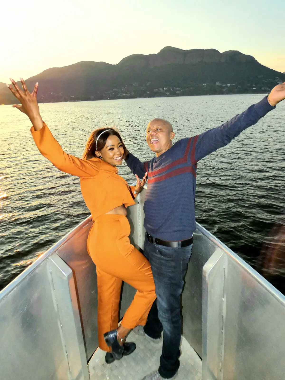 A couple on deck with their arms out at sunset